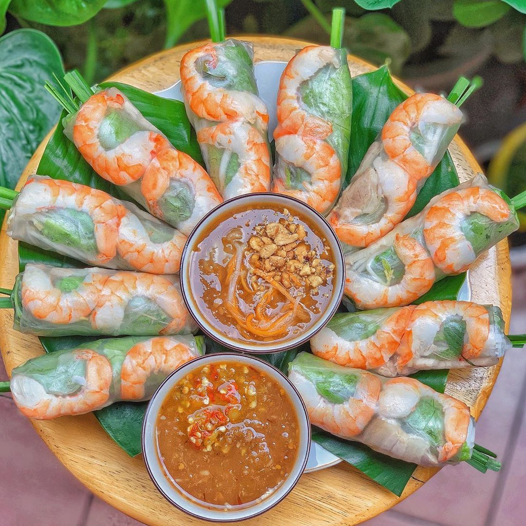 Spring rolls are presented in thin, translucent rice paper wrappers, filled with fresh pink shrimp, boiled pork, soft white rice noodles, and fresh green vegetables. The layers of ingredients are neatly arranged and visually appealing. They are best enjoyed dipped in sweet and sour fish sauce or rich, fragrant peanut sauce.