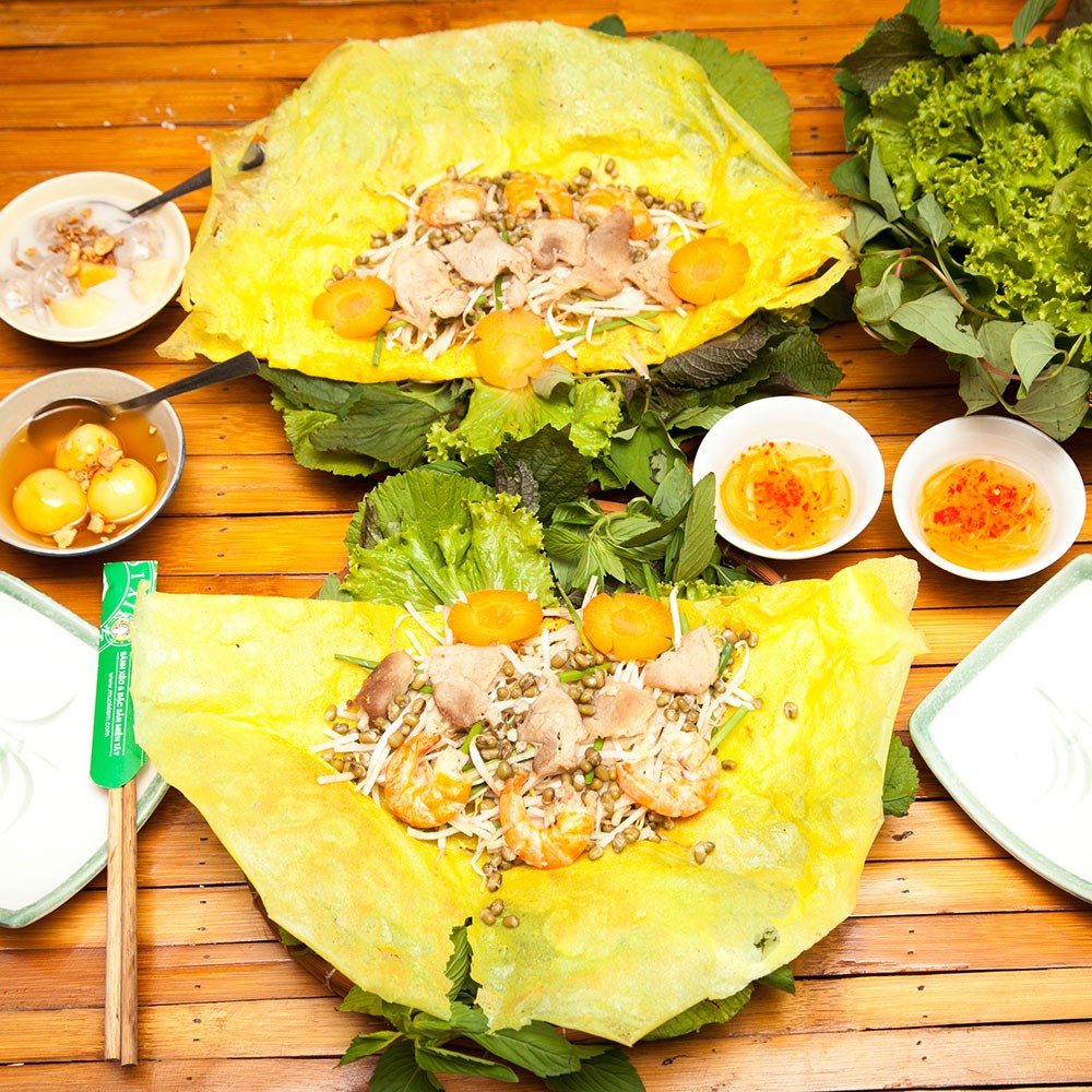 A golden-brown Vietnamese pancake, poured onto a hot pan, boasts a thin, crispy crust with a slightly charred edge for an appealing crunch. Inside is a generous filling of fresh shrimp, pork, bean sprouts, and green onions, exuding a subtle, rich aroma of rice flour and coconut milk.