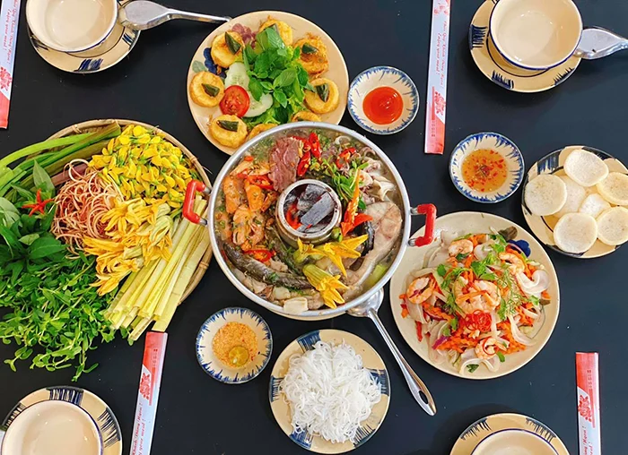The steaming hot pot of fish sauce emits a distinctive aroma, with an attractive dark brown broth made from fermented snakehead fish and other types of fish. Inside is a rich combination of shrimp, squid, fish, pork belly, and specialty vegetables from the Mekong Delta such as water lilies, water spinach, water hyacinth, and banana blossoms.